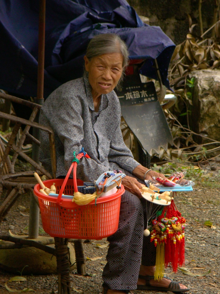 Lady sitting outside the house selling some souveniers. 